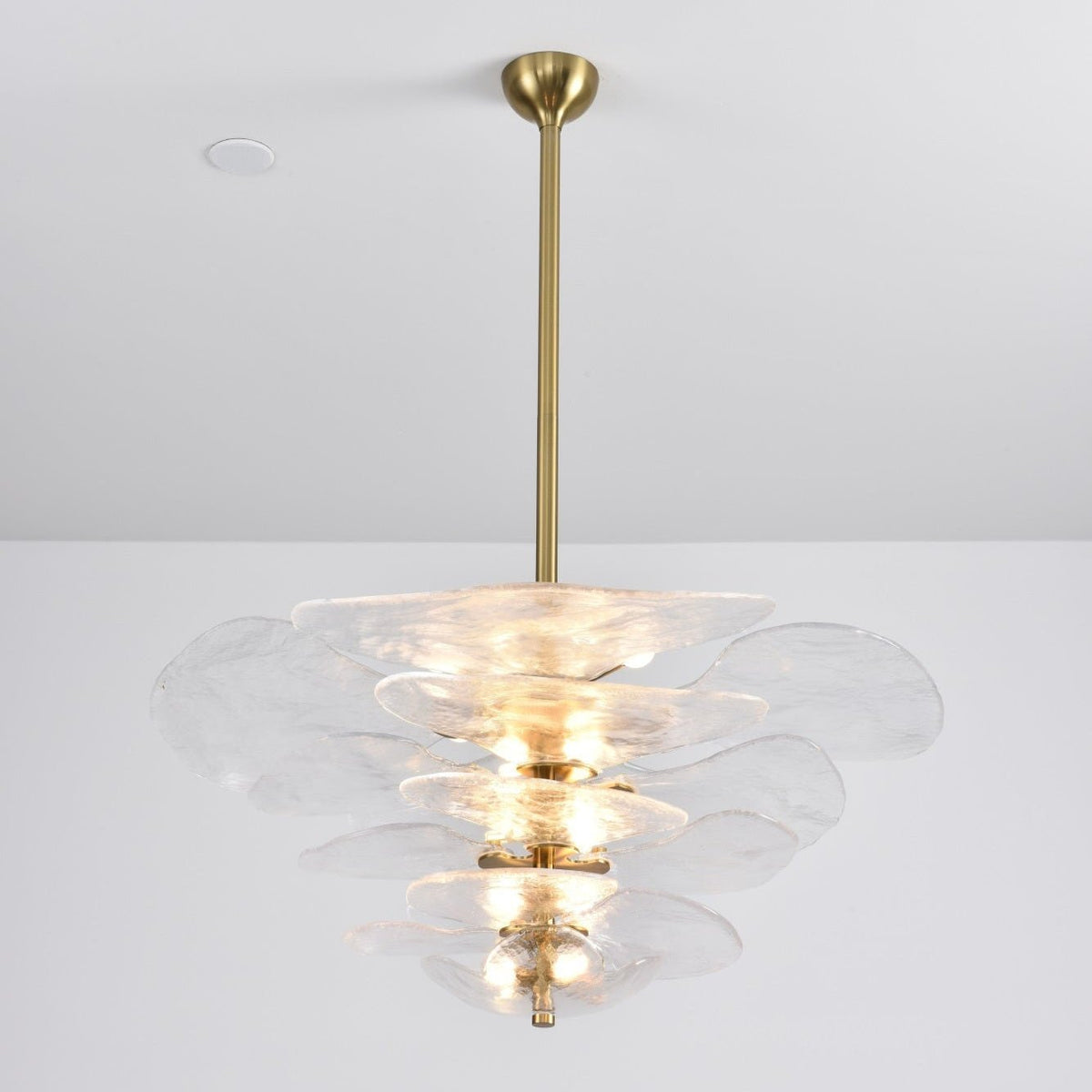 Clear Clérachic petal chandelier on a long brass rod, with lit bulbs showing through the rippled glass tiers.