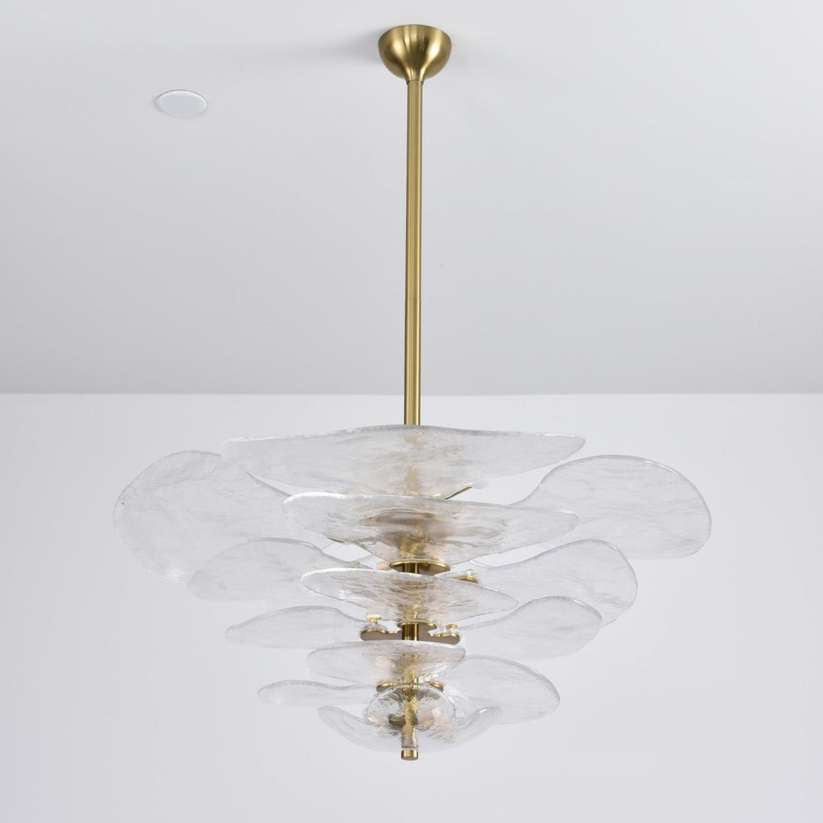 Unlit clear glass Clérachic chandelier on a long brass rod, its rippled petals stacked and a brass spindle visible in the centre.