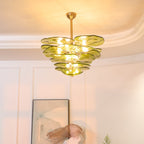 Lit green Clérachic chandelier in a room with a warm-lit coved ceiling, a large abstract print and a green fern leaf at the edge.