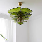 Green Clérachic chandelier seen from below near a white ceiling, with a sheer curtain and a sprig of leaves at the left.
