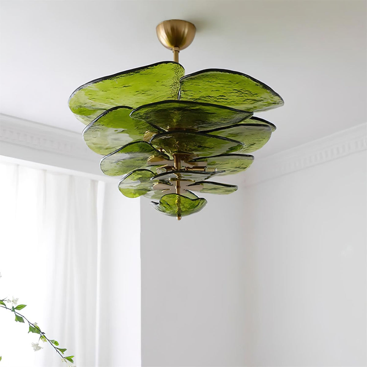 Green Clérachic chandelier seen from below near a white ceiling, with a sheer curtain and a sprig of leaves at the left.