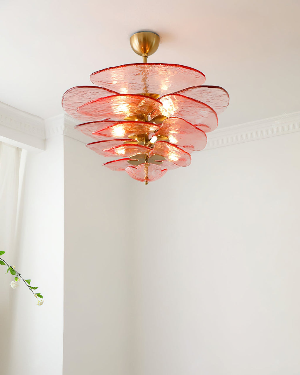 Pink Clérachic chandelier lit below a white ceiling, with a sheer curtain and a sprig of blossom to the left.