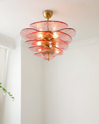 Pink Clérachic chandelier lit below a white ceiling, with a sheer curtain and a sprig of blossom to the left.