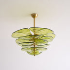 Unlit green Clérachic chandelier on a white backdrop, its olive glass petals layered below a short brass rod and cup.