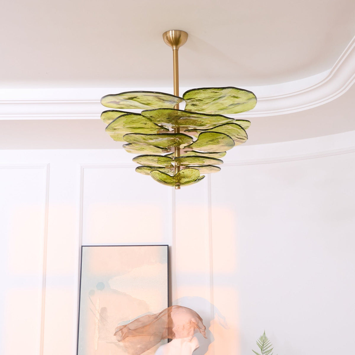 Lit green Clérachic chandelier near a coved ceiling, with an abstract print and a plaster sculpture on a cabinet below.