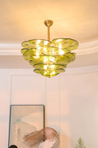 Narrow view of a lit green Clérachic chandelier below a coved ceiling, with a framed print and a sculpture beneath.