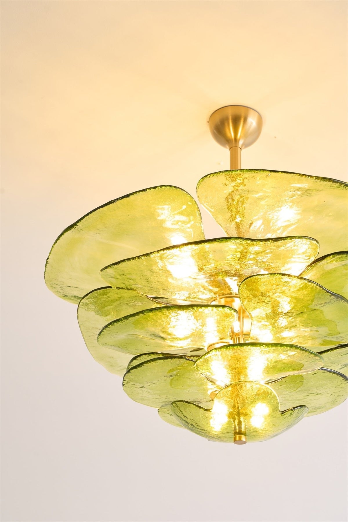 Close crop of a lit green Clérachic chandelier, showing the rippled olive glass petals and the glow of the bulbs between them.