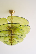 Close crop of the green glass petals and brass spindle on this Clérachic chandelier, lit by daylight against a white ceiling.