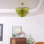 Small green Clérachic chandelier high in a curved white room, above a framed print and a cabinet with a cane panel.