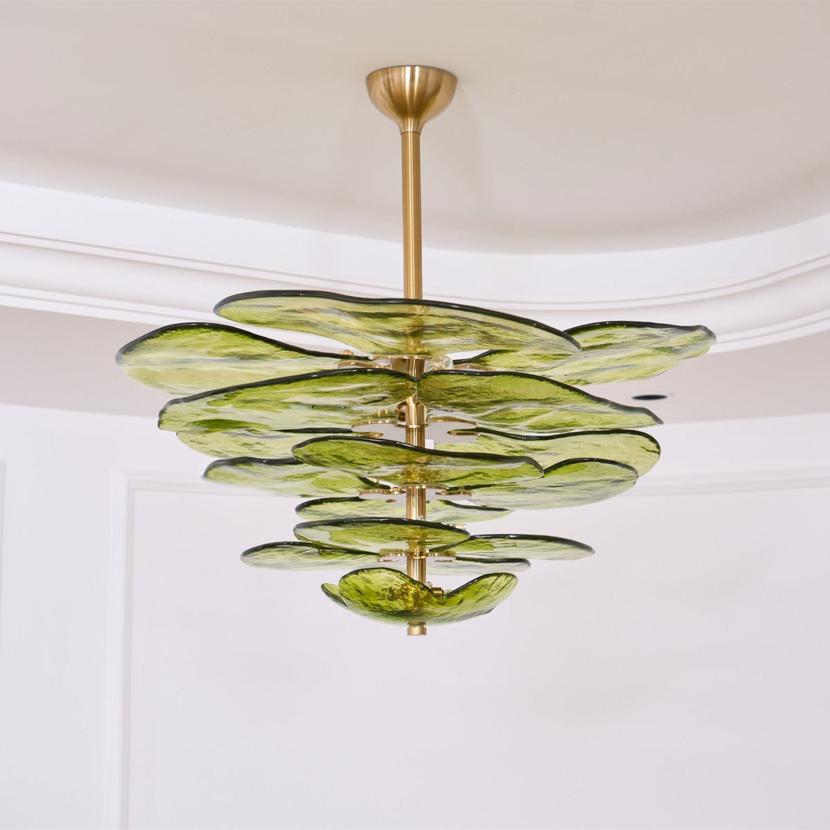 Wide green Clérachic chandelier hanging below a coved ceiling, its glass petals spread in tiers around a brass rod.