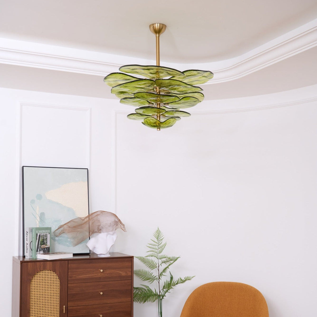 Unlit small green Clérachic chandelier in a curved white room, with a framed print and a plaster sculpture on the cabinet below.