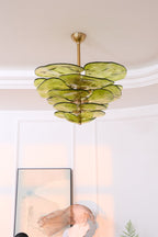 Unlit green Clérachic chandelier below a coved ceiling, with a framed print and a pink glass sculpture partly in view beneath.