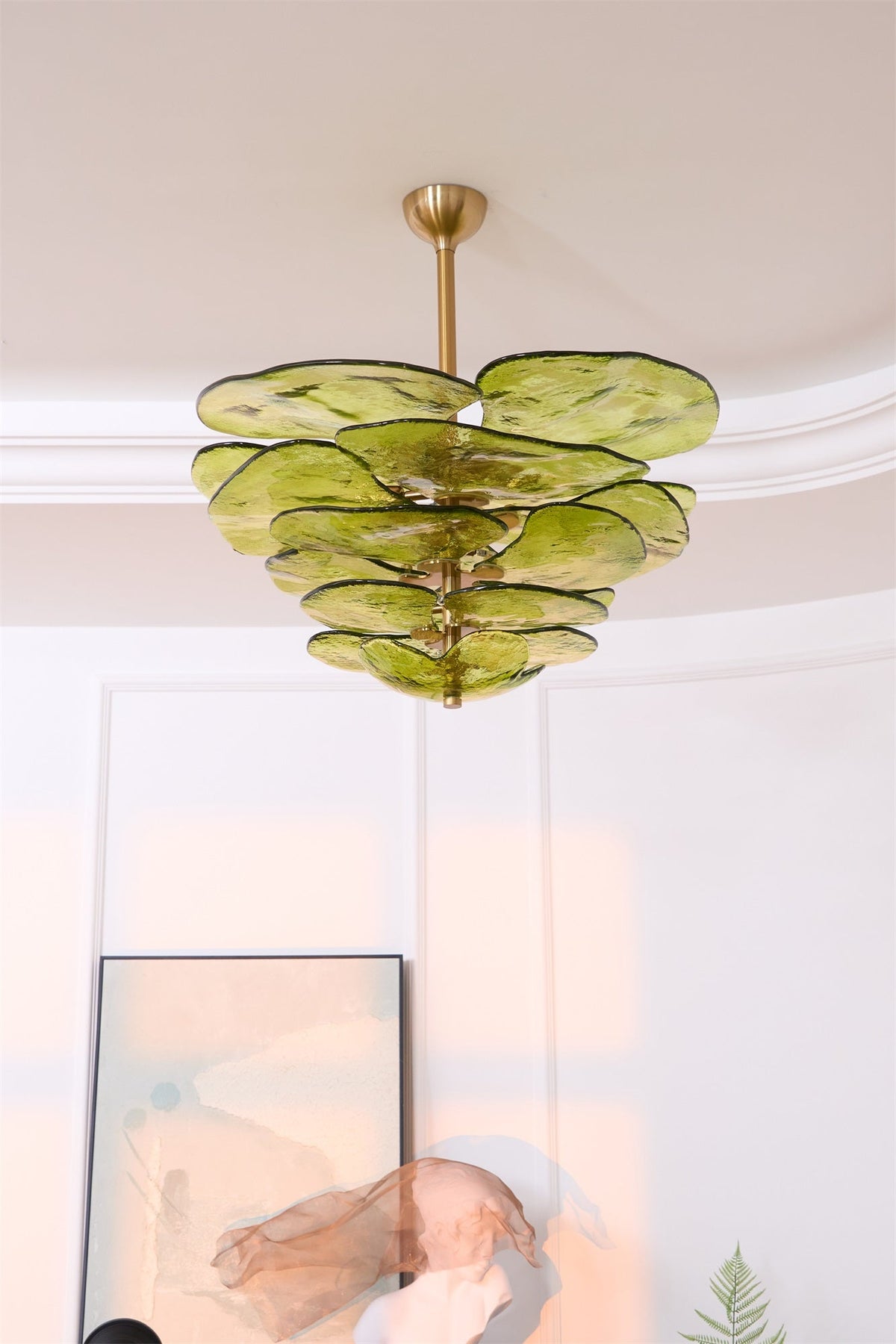 Unlit green Clérachic chandelier below a coved ceiling, with a framed print and a pink glass sculpture partly in view beneath.