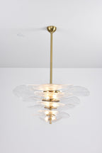 Lit clear glass Clérachic chandelier on a long brass rod, with a bright glow at its centre against a pale grey backdrop.