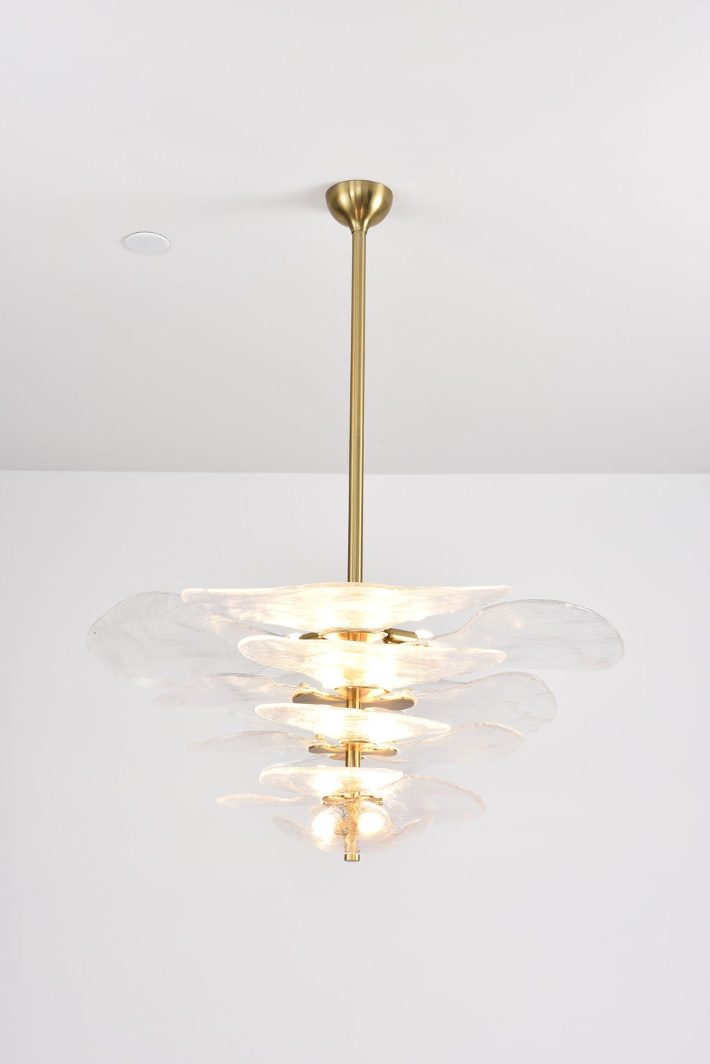 Clear glass Clérachic chandelier lit brightly on a grey backdrop, its pale tiers glowing from the bulbs inside.