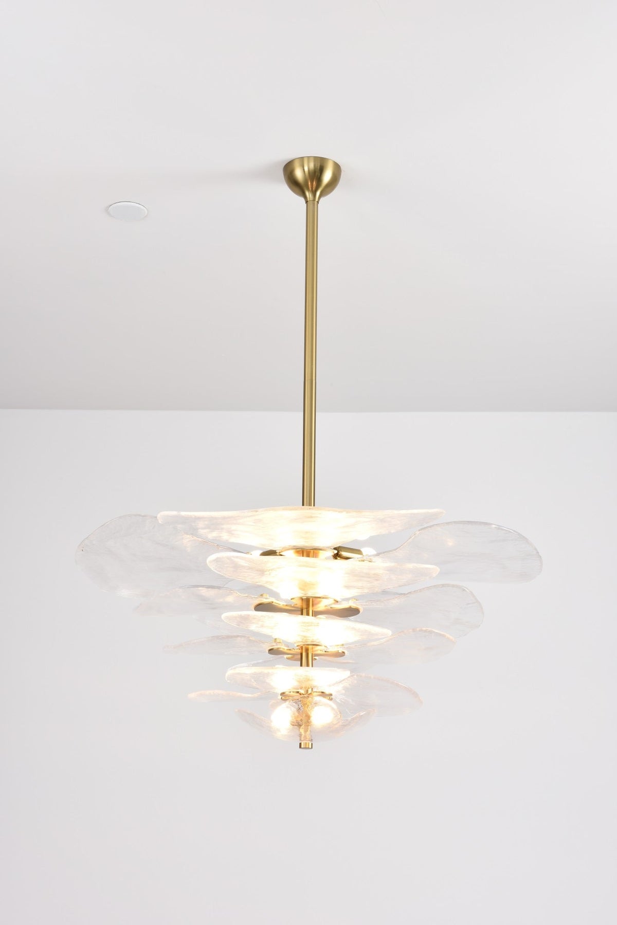 Clear glass Clérachic chandelier lit brightly on a grey backdrop, its pale tiers glowing from the bulbs inside.