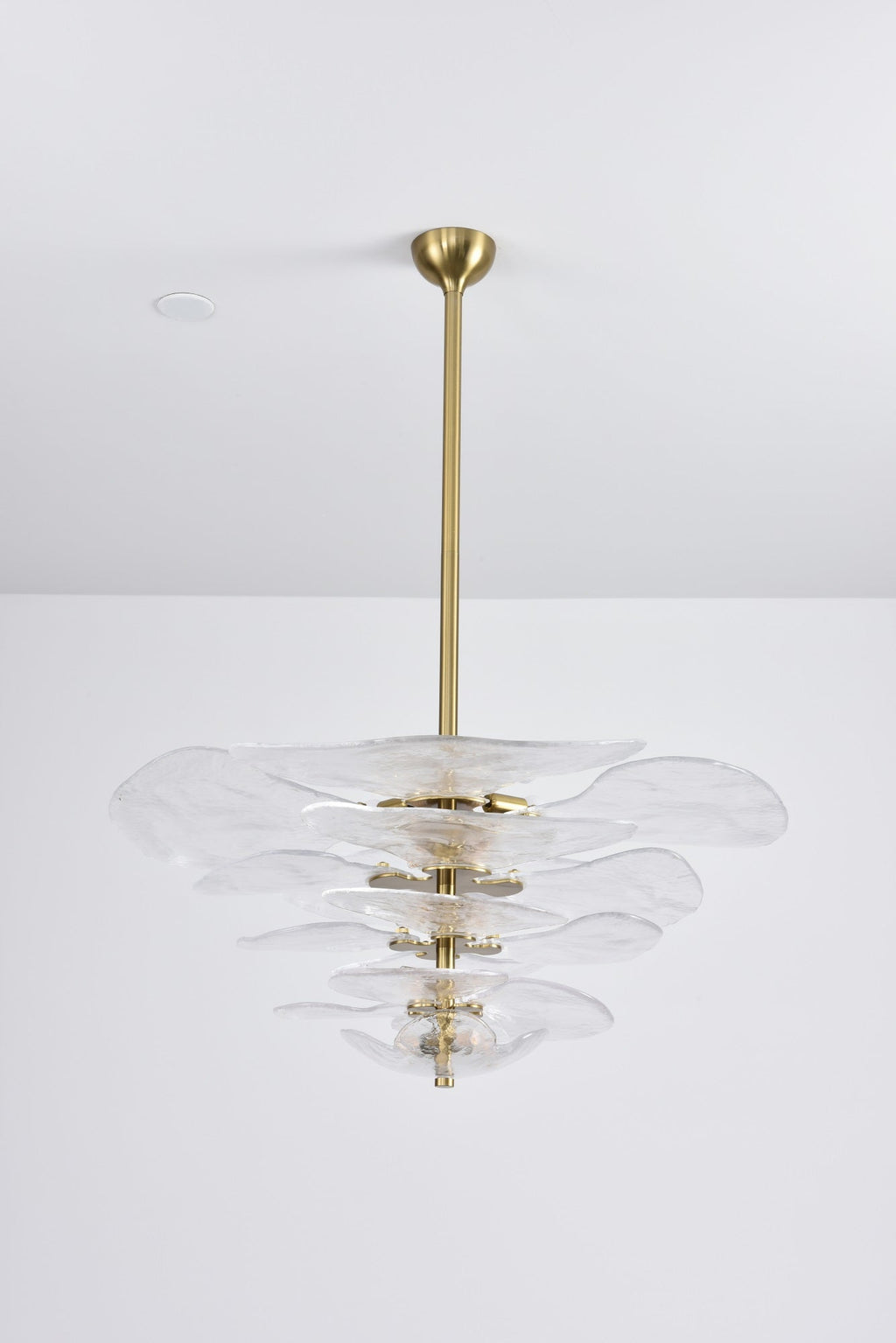 Unlit clear glass Clérachic chandelier with gold fittings on a grey backdrop, its tiers of petals hung from a long brass rod.