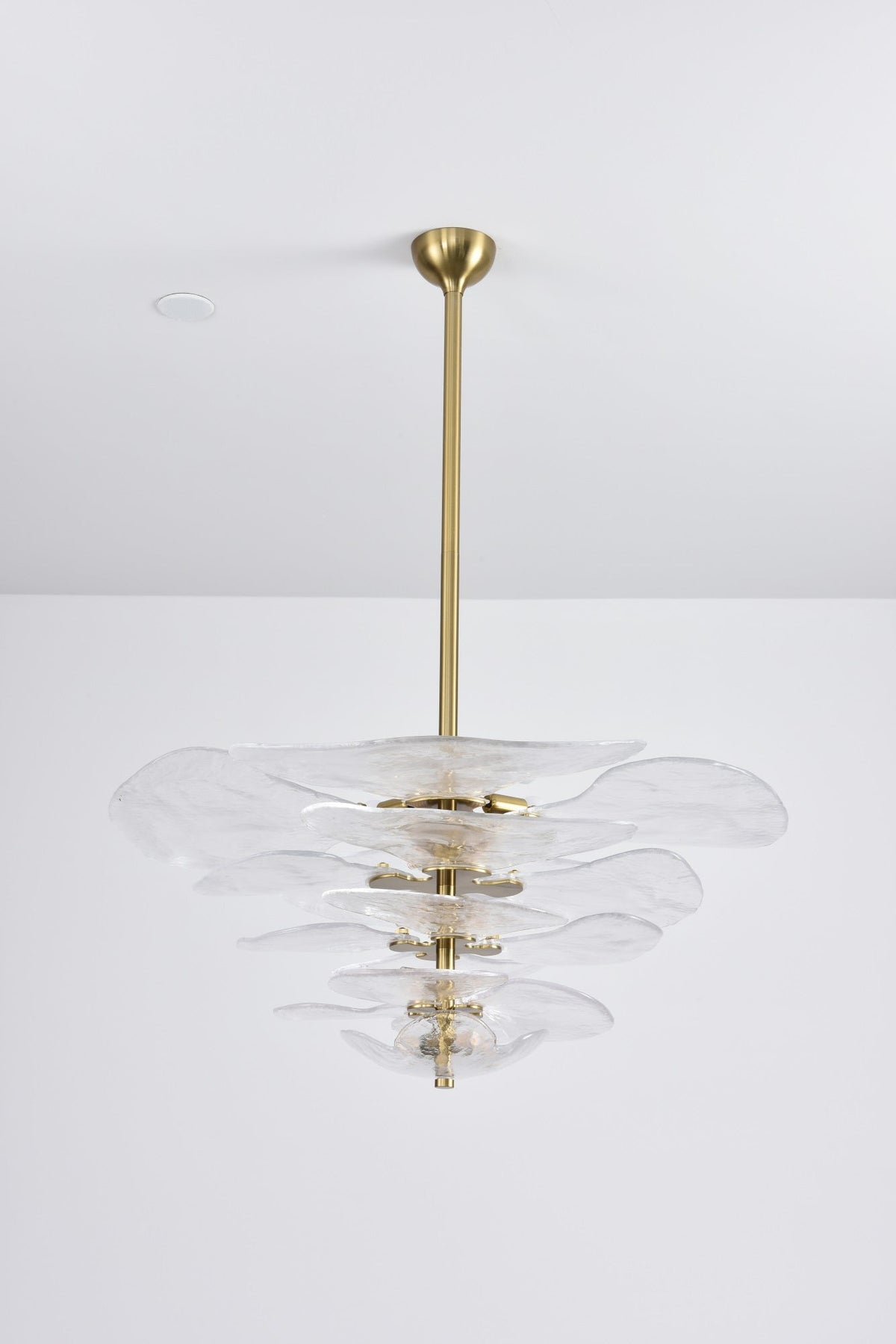 Unlit clear glass Clérachic chandelier with gold fittings on a grey backdrop, its tiers of petals hung from a long brass rod.