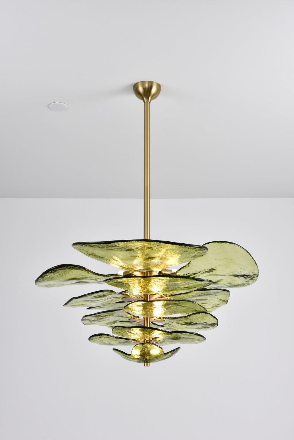 Green Clérachic chandelier on a long brass rod, lit softly, with olive glass petals of varied sizes on a grey backdrop.