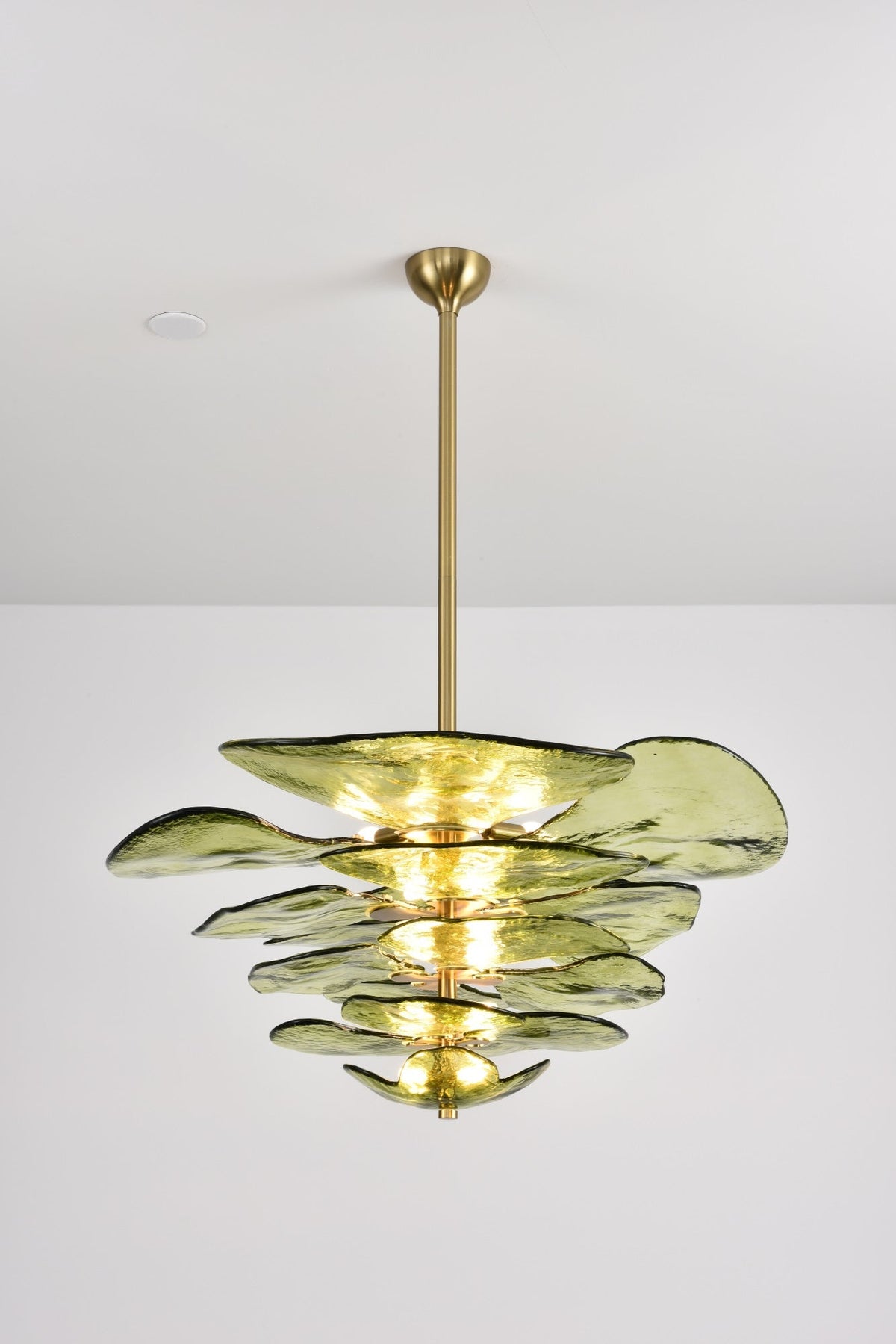 Brightly lit green Clérachic chandelier on a long brass rod, with light glowing between each layer of olive glass.