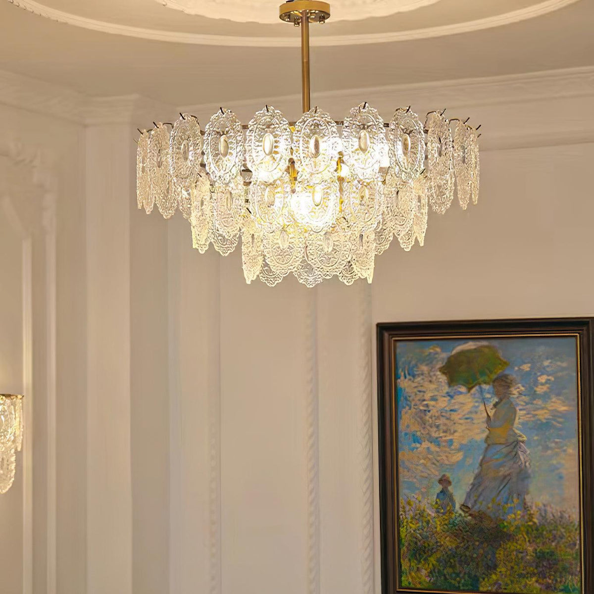 Lit Clérachic glass pendant on a gold rod, beside a cream panelled wall and a framed painting of a figure with a green parasol.