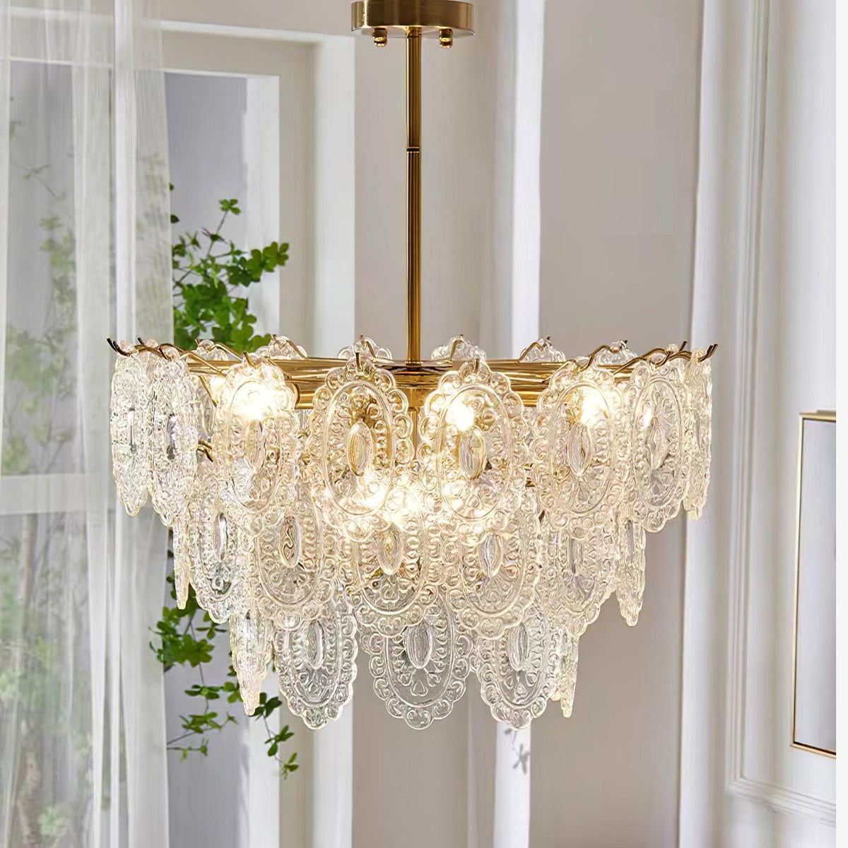 Close, side-on view of the Clérachic pendant's lit, diamond-textured glass shades, with a leafy plant and white curtains behind.