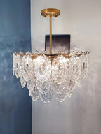 Clérachic glass pendant on a gold rod, lit against a blue-grey plastered wall, with a small dark frame behind it.
