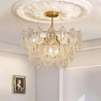Lit Clérachic pendant with warm bulbs showing through its glass panels, below an ornate white ceiling rose and above a framed portrait.
