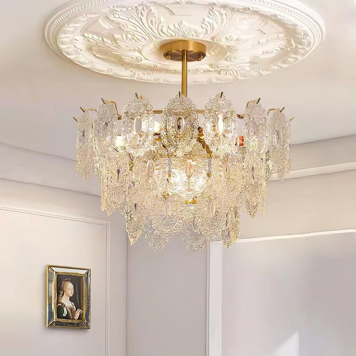 Lit Clérachic pendant with warm bulbs showing through its glass panels, below an ornate white ceiling rose and above a framed portrait.