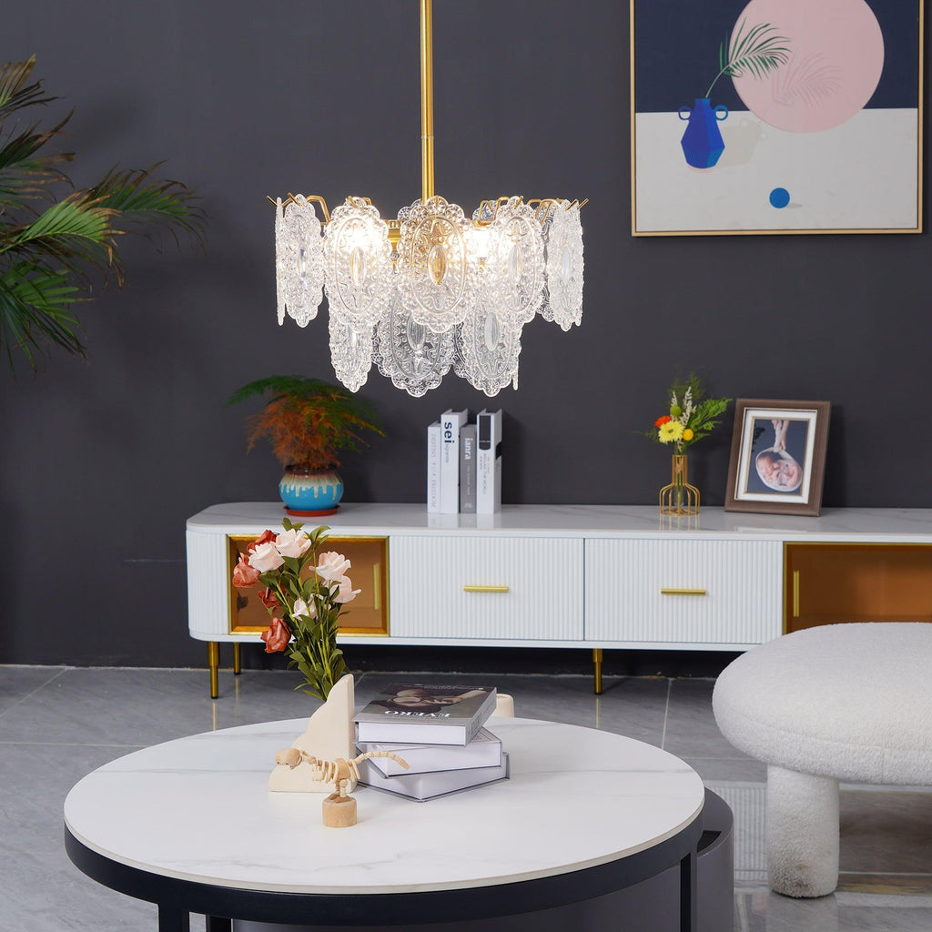 A small Clérachic glass pendant hangs above a white round table with books and flowers, in front of a dark grey wall and a low media unit.