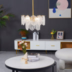 A small Clérachic glass pendant hangs above a white round table with books and flowers, in front of a dark grey wall and a low media unit.