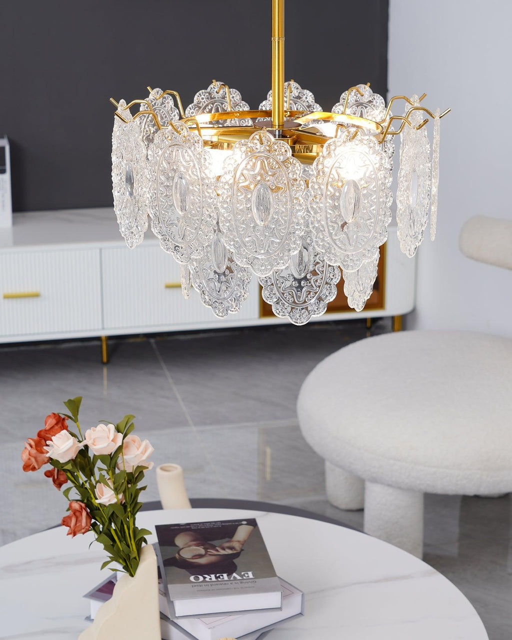 Close-up of the Clérachic pendant's lit glass shades, with a stack of books and orange-pink flowers on a marble table below.