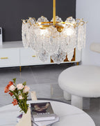 Close-up of the Clérachic pendant's lit glass shades, with a stack of books and orange-pink flowers on a marble table below.