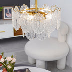 Tilted view from below of this Clérachic pendant, its gold ring and bulbs visible through clear glass, above a white boucle chair.