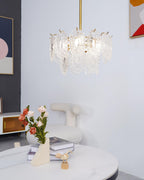 Compact Clérachic glass pendant lit above a white marble table and a vase of roses, with a framed print and a boucle chair beside it.