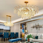 A large Clérachic glass pendant and a smaller linear fixture lit in an open-plan living and dining room with blue dining chairs.