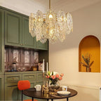 Clérachic pendant lit above a small round table with a candle, flowers and cups, in front of green kitchen cabinets and an arched niche.