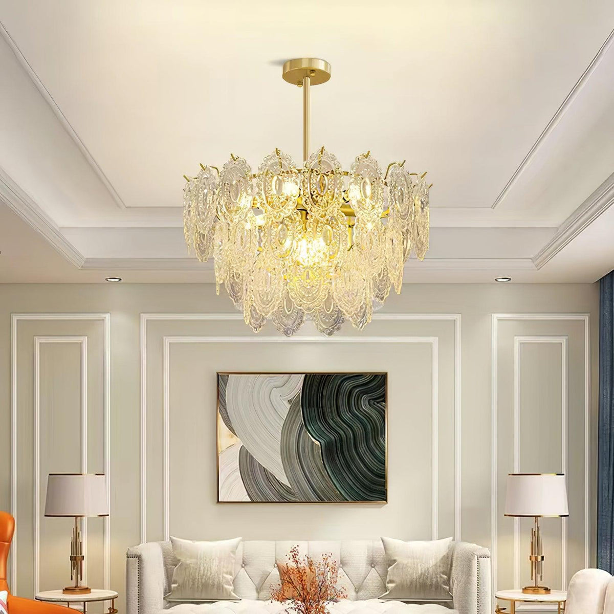 Clérachic gold-stemmed glass pendant in a living room with a tray ceiling, over a cream sofa and two white table lamps.