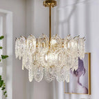 Clérachic pendant on a gold rod beside a pale wall, with a framed picture of a woman and tall plants in view.