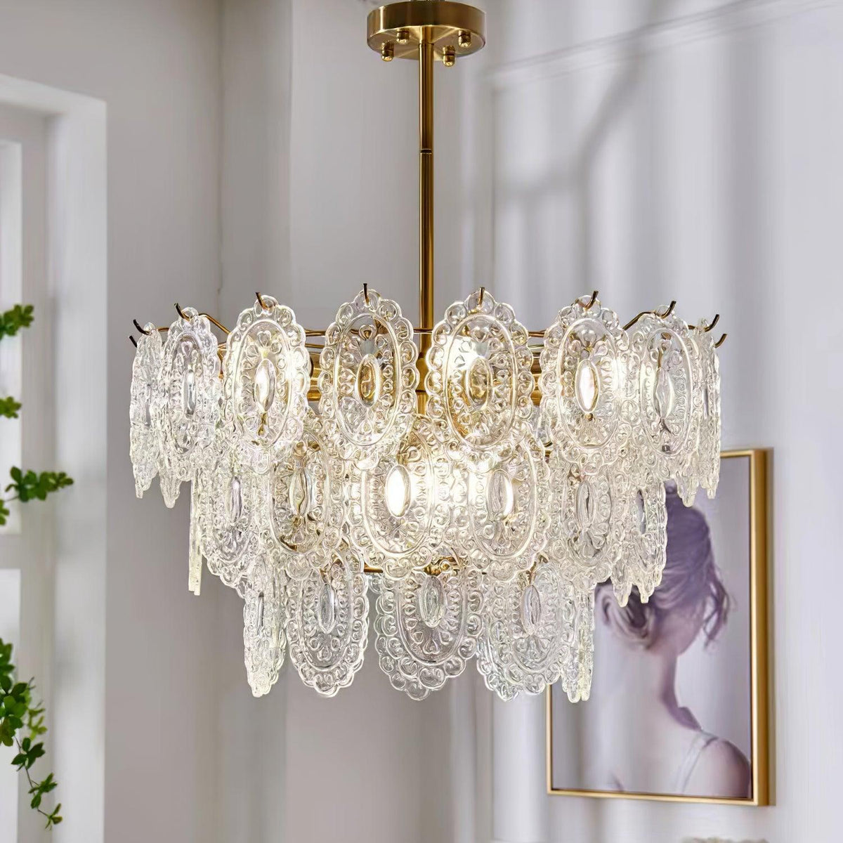 Clérachic pendant on a gold rod beside a pale wall, with a framed picture of a woman and tall plants in view.