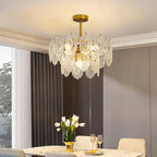 Clérachic pendant lit over a marble dining table set with glasses and white tulips, near tall grey curtains.