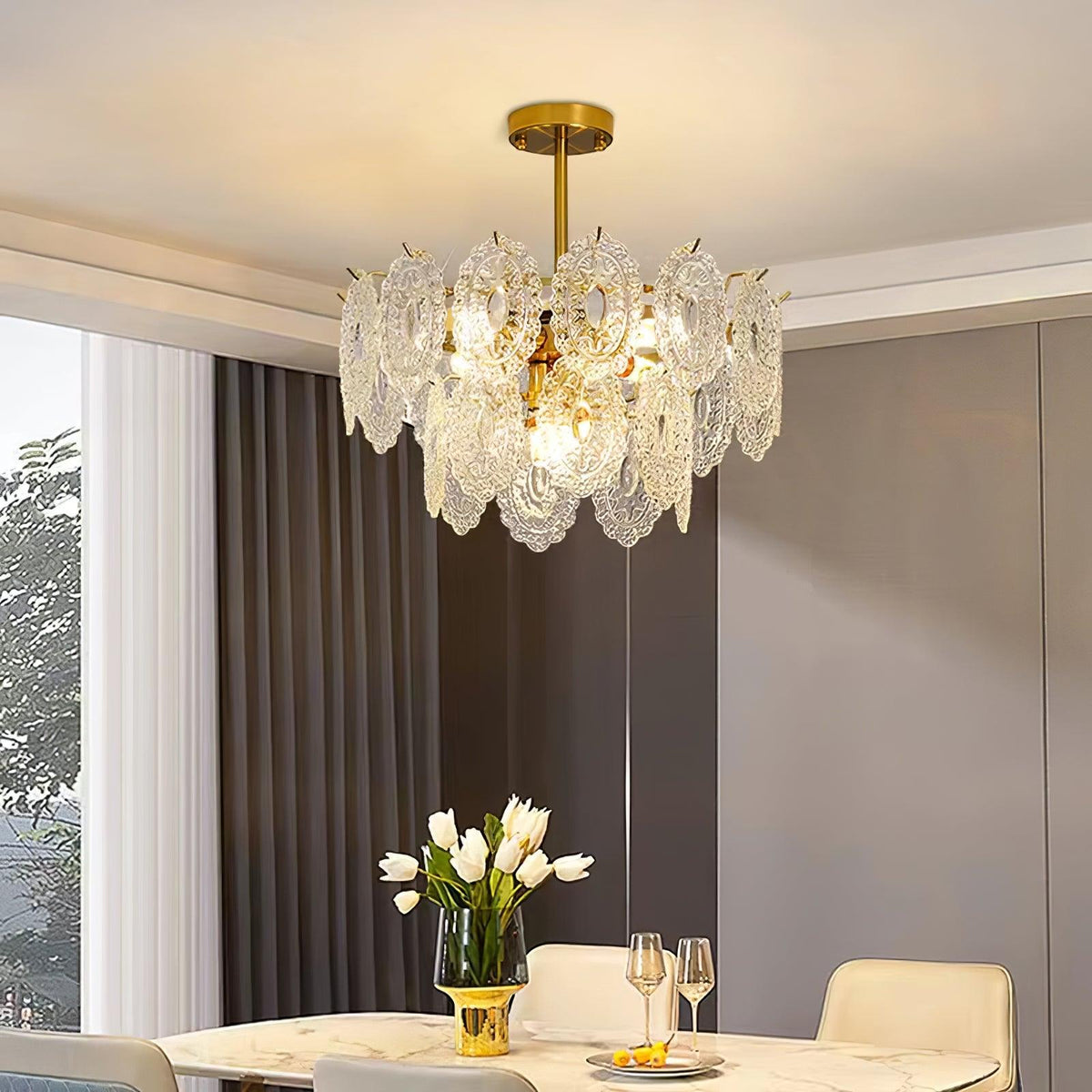 Clérachic pendant lit over a marble dining table set with glasses and white tulips, near tall grey curtains.