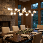 Clérachic gold-branch chandelier glowing over a long wooden dining table, with a stone fireplace and tall windows beyond.
