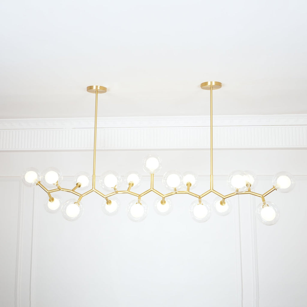 Lit Clérachic chandelier with many glowing globes on gold branches, hung from two rods below a white panelled ceiling edge.