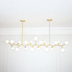 Lit Clérachic chandelier with many glowing globes on gold branches, hung from two rods below a white panelled ceiling edge.