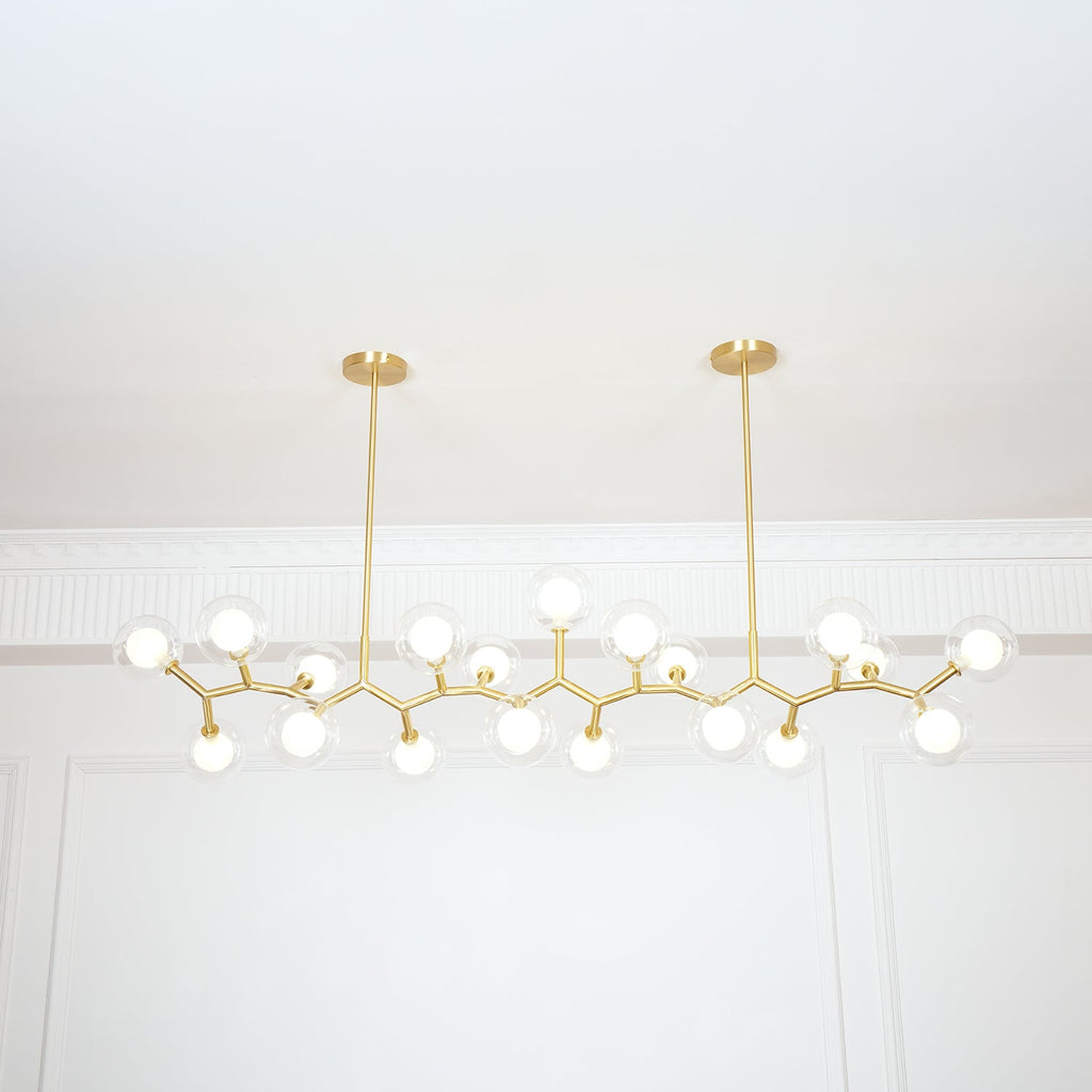 Clérachic gold-branch chandelier with its globes lit, hanging from two short rods in front of a white wall with moulding.
