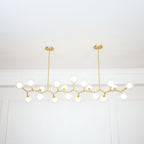 Clérachic gold-branch chandelier with its globes lit, hanging from two short rods in front of a white wall with moulding.