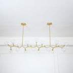 Unlit Clérachic chandelier with clear globes on thin gold branches, seen from slightly below under a white cornice.