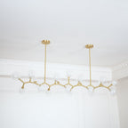 Clérachic chandelier with clear glass globes on gold branches, seen unlit beside a white panelled wall and ceiling moulding.