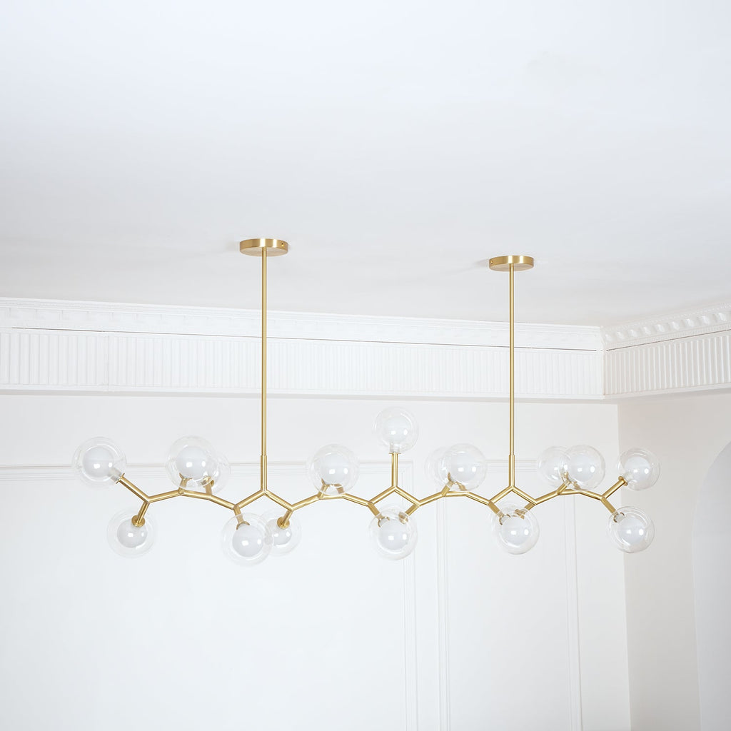 Unlit Clérachic chandelier with clear globes along a gold frame, hung from two rods in a corner with a white cornice.
